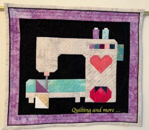 Pieced quilt showing a sewing machine with spools of thread and a pin cushion.