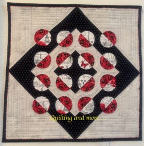 Split circles (red/white) are set into off-white and black background, the resulting blocks forming an on-point black square surrounded by large off-white triangles. Fabric is poppies and Paris-themed.