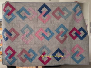 Overall view of quilt with white background set with interlocking pairs of hollow squares on point in blues and pinks.