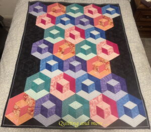 Quilt with colorful blocks in shades of teal, pink, orange, purple, and blue giving a dimensional box-like effect and set on a black background.