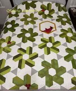 Quilt with "leaf" blocks in shades of green set on white with grey accents. One block shows a pieced red cardinal sitting on the block's gold border.